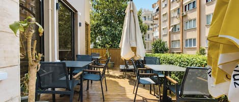 An outdoor patio area with tables and chairs, surrounded by a wooden deck, and adjacent to a building with multiple windows.