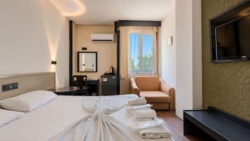 A hotel room with a large bed, a desk, a chair, a television, and a window with curtains.