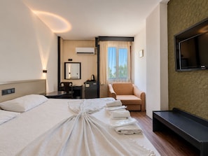 Habitación de hotel con una cama grande, un escritorio, una silla, un televisor y una ventana con cortinas.