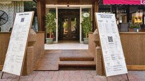 Entrada de un restaurante con fachada de madera, dos macetas y un atril con la carta.