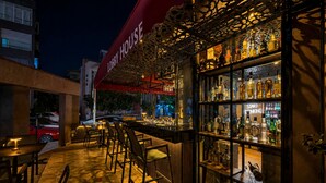 Zona de bar al aire libre con toldo rojo, mobiliario de madera y una variedad de botellas a la vista.