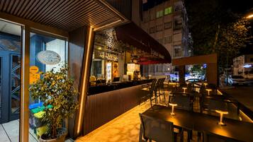 An outdoor seating area with tables and chairs, a bar counter, and a potted plant.