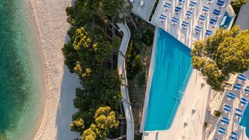 An aerial view of a beach resort with a pool, lounge chairs, and a pathway leading to the beach.