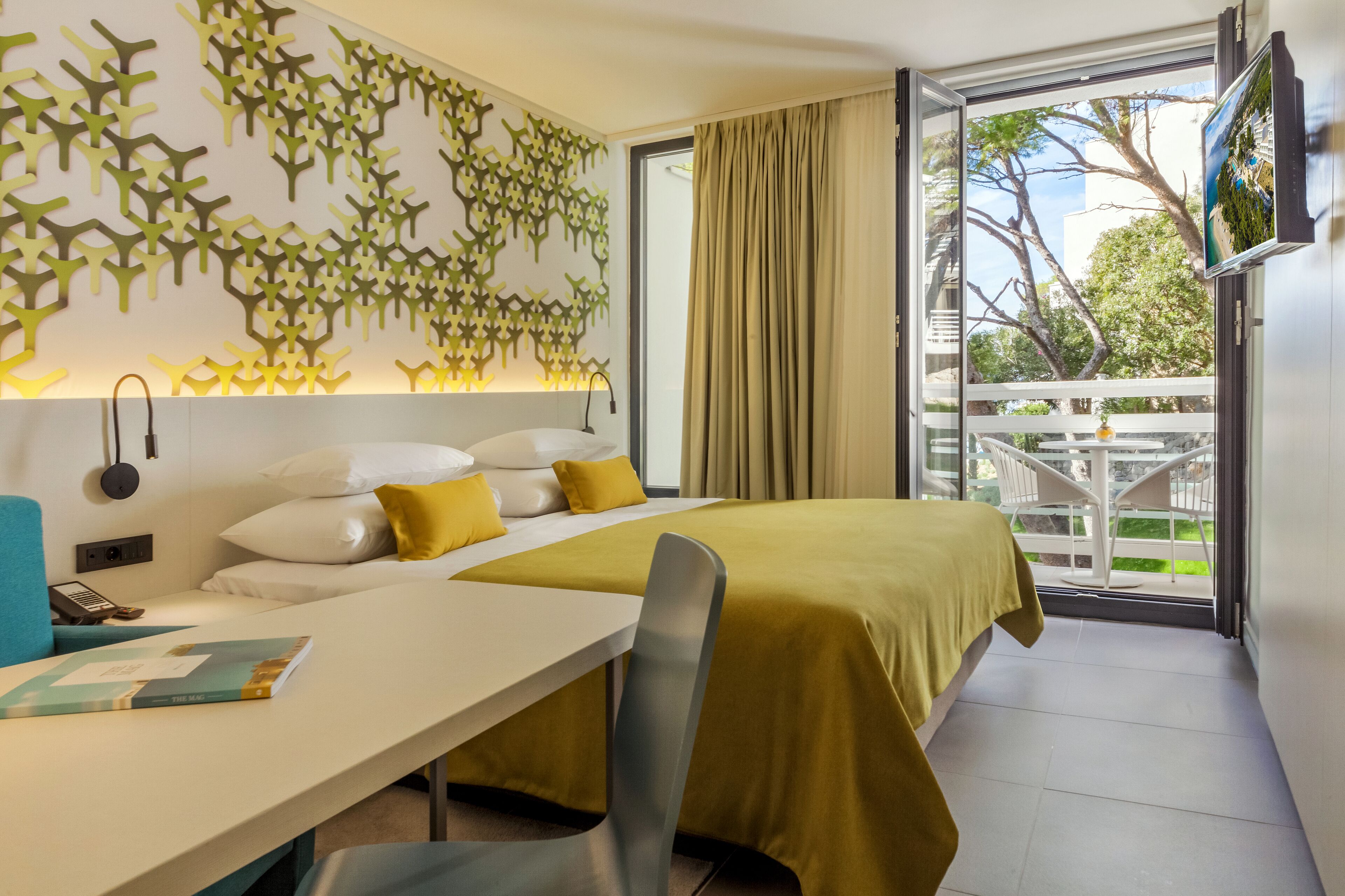 A hotel room with a bed, a desk, and a view of the outdoors.