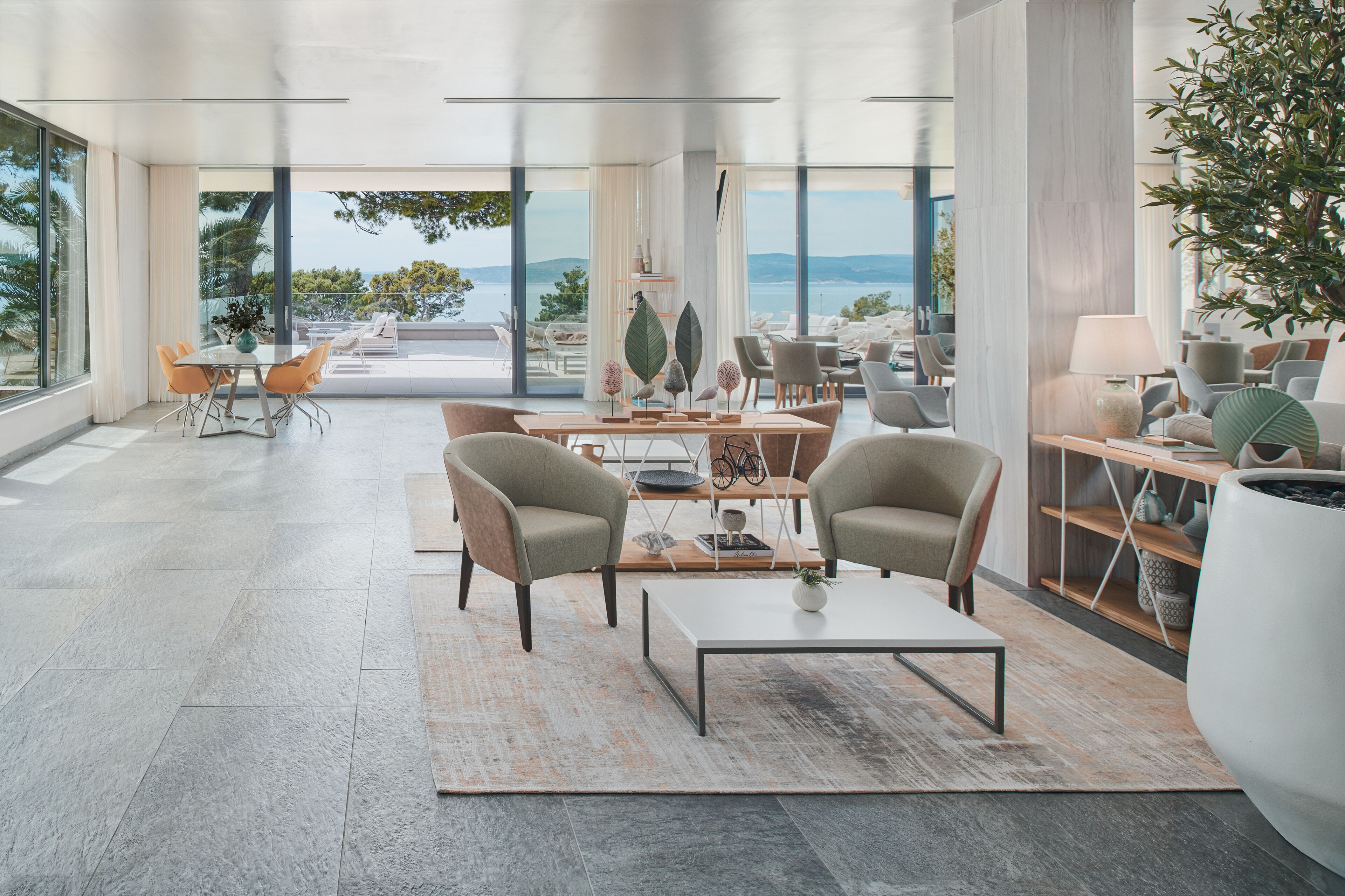 A spacious, modern living area with a large window overlooking a scenic view. There are comfortable seating arrangements, a coffee table, and a bookshelf.