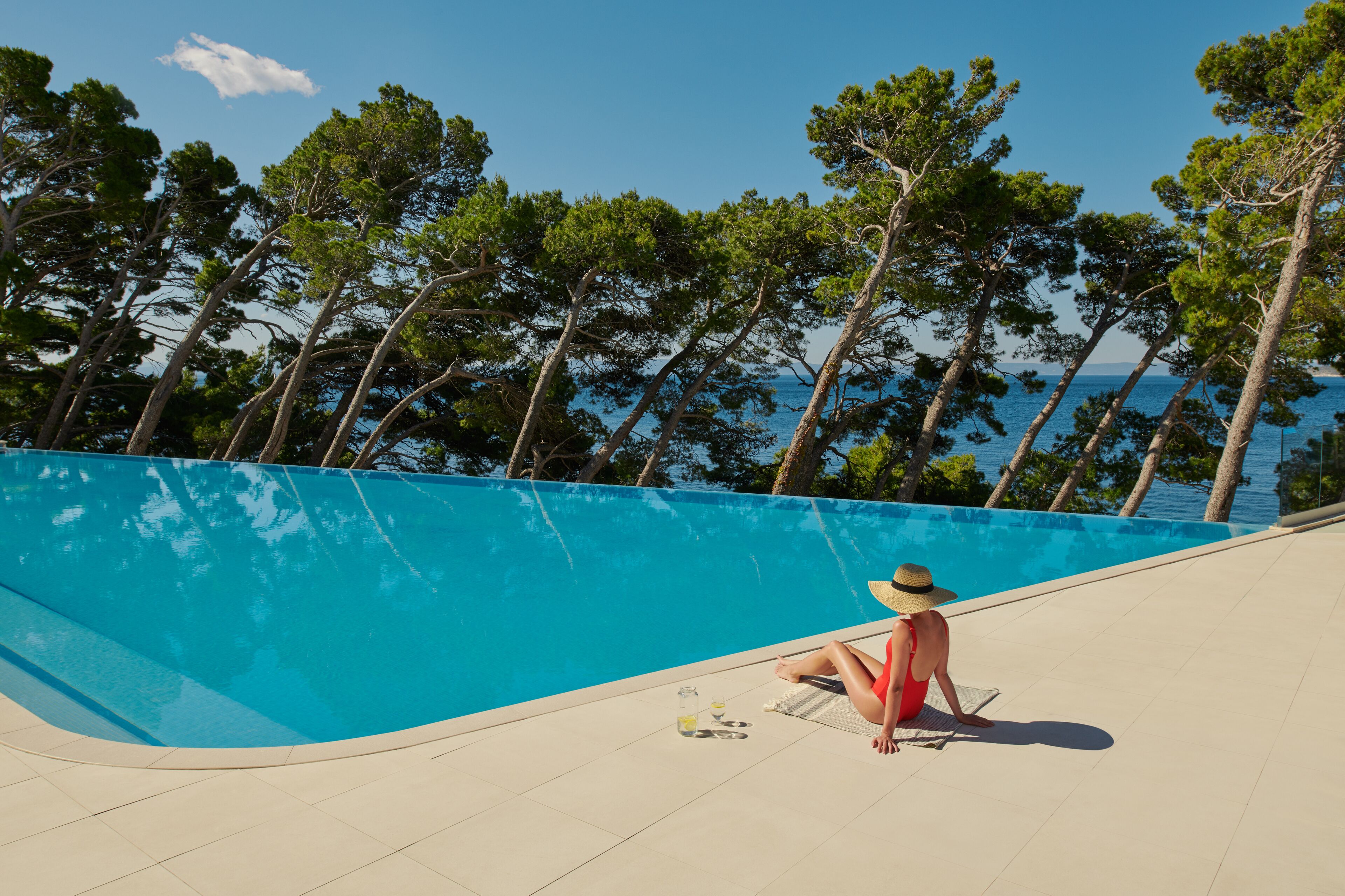 Una persona sentada junto a una piscina con vistas a árboles y agua.