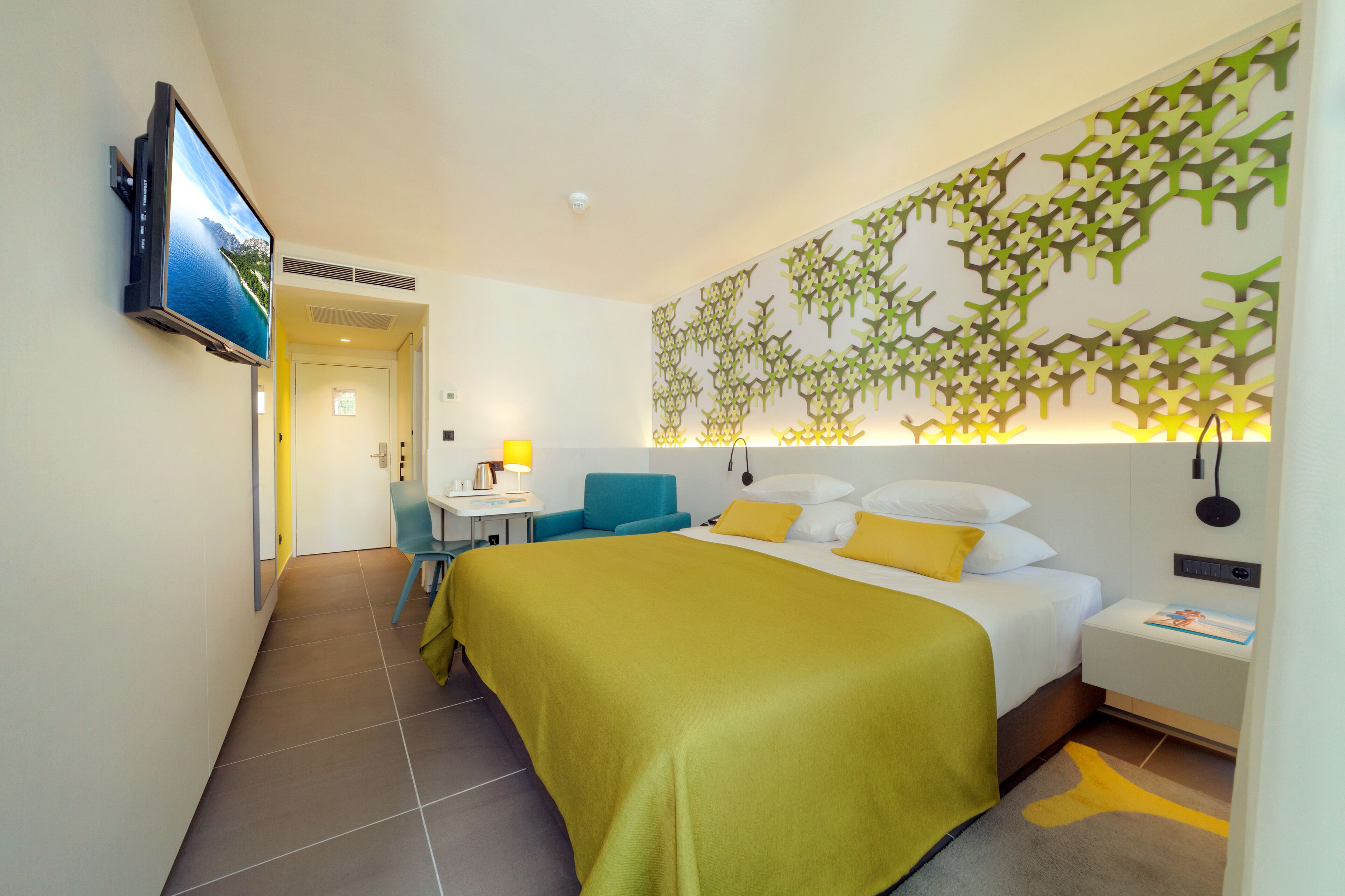 A hotel room with a bed, a desk, a chair, and a TV mounted on the wall.