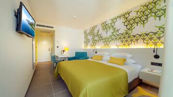 A hotel room with a bed, a desk, a chair, and a TV mounted on the wall.