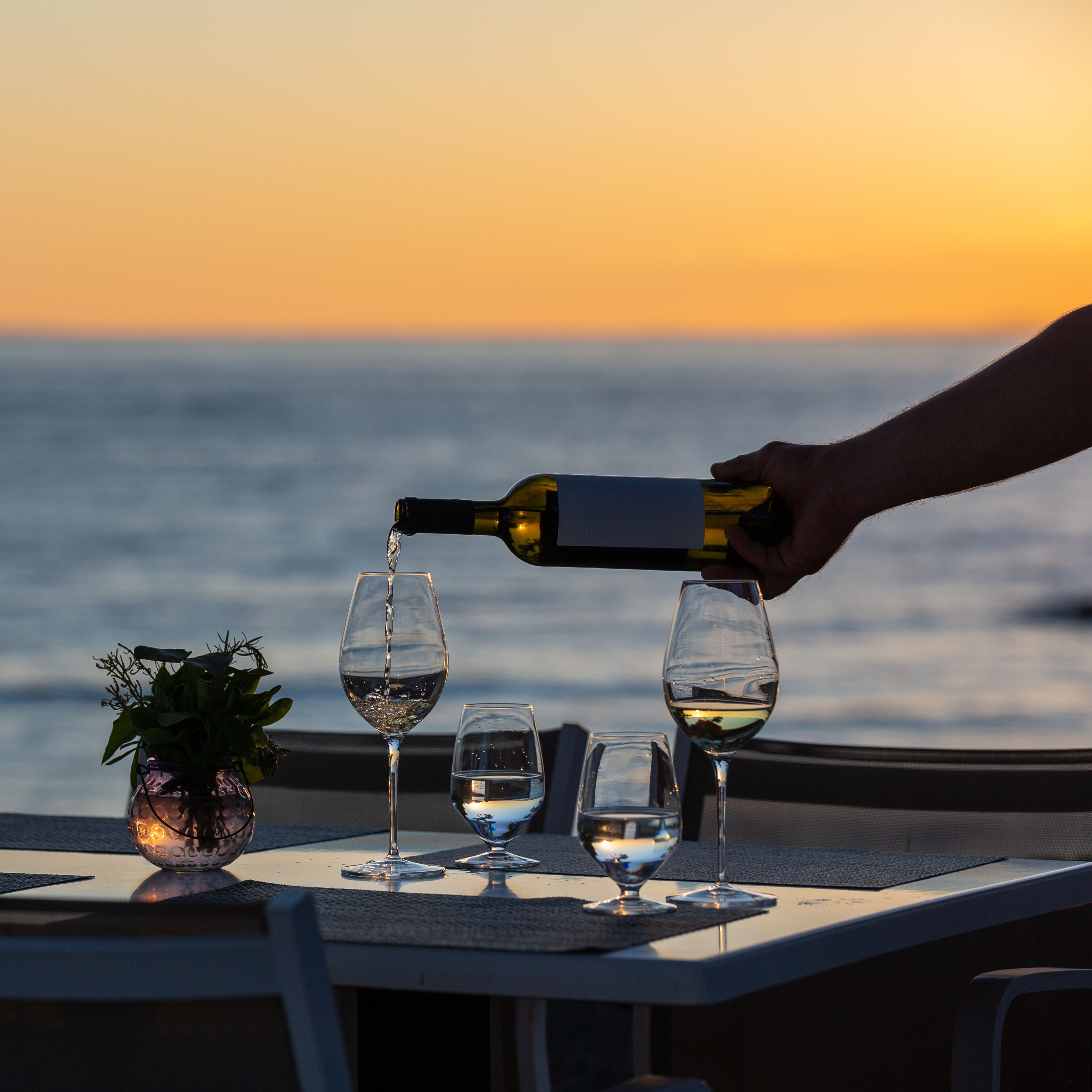 Una mesa con tres copas de vino y una botella siendo servida en una de ellas.