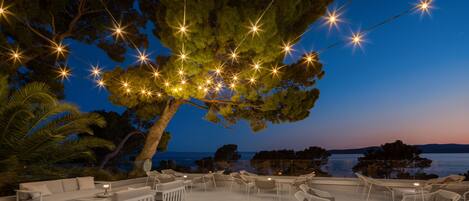 An outdoor seating area with white furniture and string lights, overlooking a body of water.