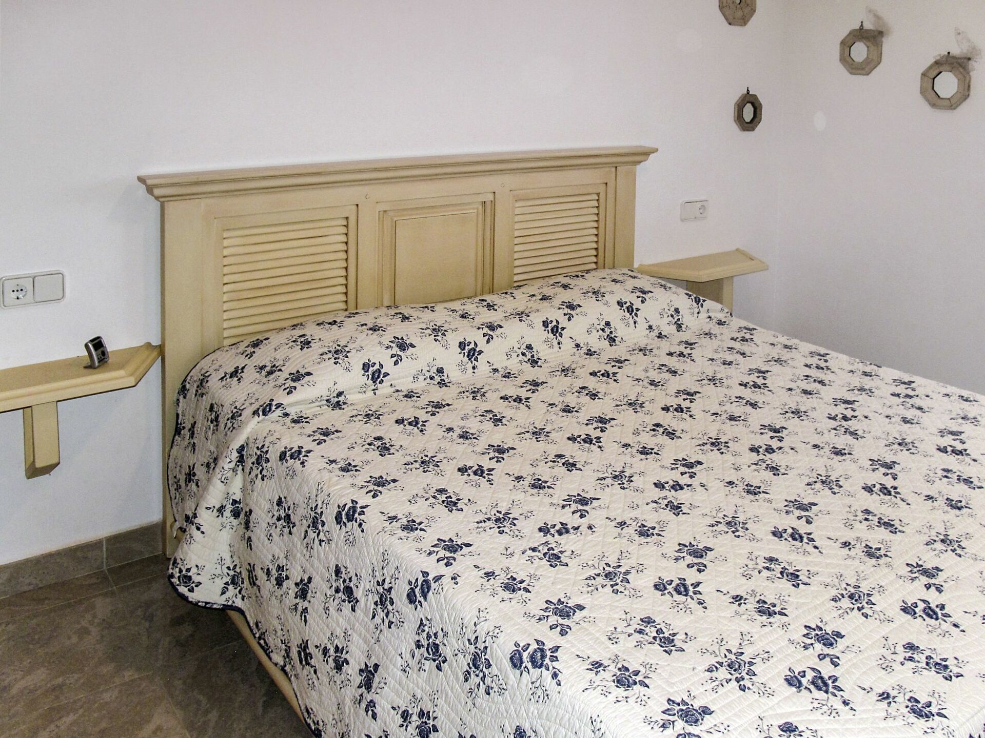 Un dormitorio con cama, cabecero de madera, mesita de noche y un reloj en la pared.