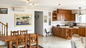 A spacious living area with a wooden dining table and chairs, a kitchen with wooden cabinets and a built-in island, and a cozy seating area with a striped sofa.