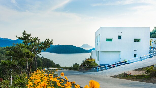 A modern white building with a view of a lake and mountains. - Sosiega Hue Pension (Goheung)
