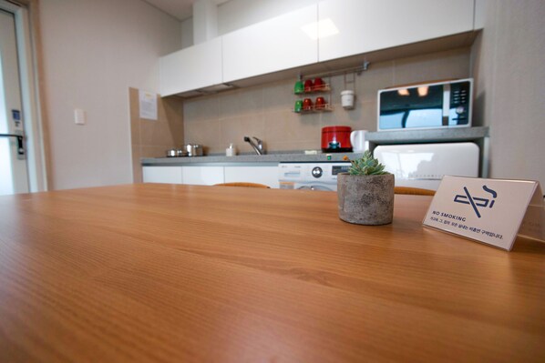 A wooden table with a sign indicating no smoking. In the background, there is a kitchen area with a microwave, a stove, and various kitchen items. - Sosiega Hue Pension (Goheung)