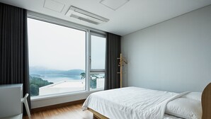A modern hotel room with a large window, wooden flooring, and a neatly made bed. - Sosiega Hue Pension (Goheung)