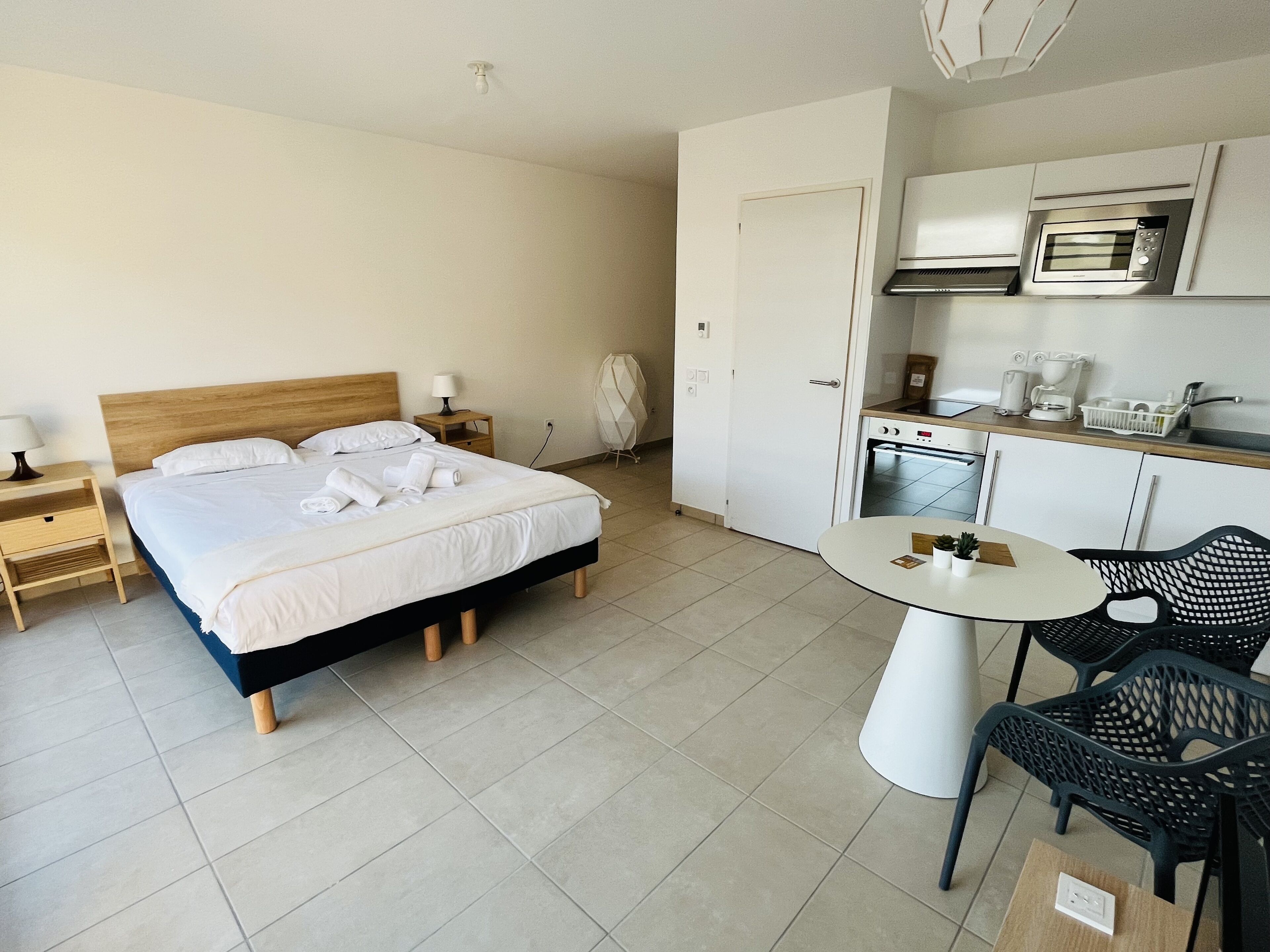 A hotel room with a bed, bedside table, lamp, and a kitchenette with a microwave and coffee maker.