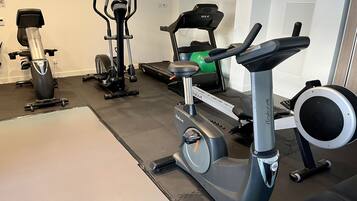 Un gimnasio en casa con varios equipos de ejercicio, incluyendo una elíptica, una bicicleta estática y una cinta de correr.