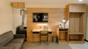 A modern room with a sofa, a desk with a chair, a television mounted on the wall, and a wooden cabinet. - L Meridian Suites (Zamboanga)