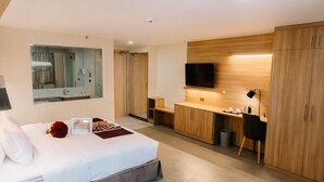 A modern hotel room with a large bed, a desk, a TV, and wooden cabinets. - L Meridian Suites (Zamboanga)