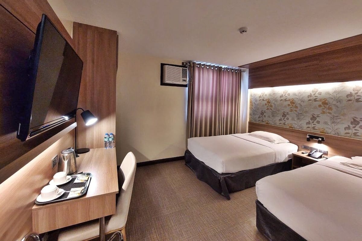 A hotel room with two beds, a desk with a chair, a TV, and a window with curtains.
