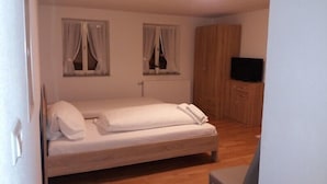 A bedroom with a wooden bed, two windows with curtains, a radiator, a wardrobe, and a television. - Apartments B & B27 (Rottweil)