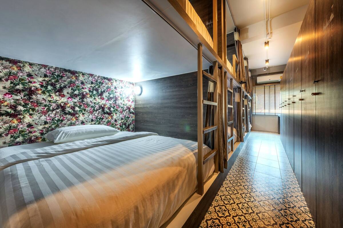 Quarto de hotel moderno com uma cama grande, papel de parede floral e um guarda-roupa de madeira.