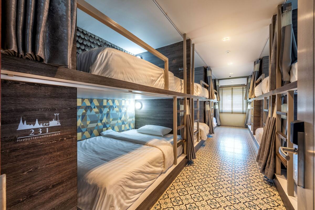 Quarto de hotel com beliches, piso estampado e um mural com vista da cidade.