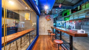 Uma área de bar com banquetas de madeira, um balcão e um letreiro neon.