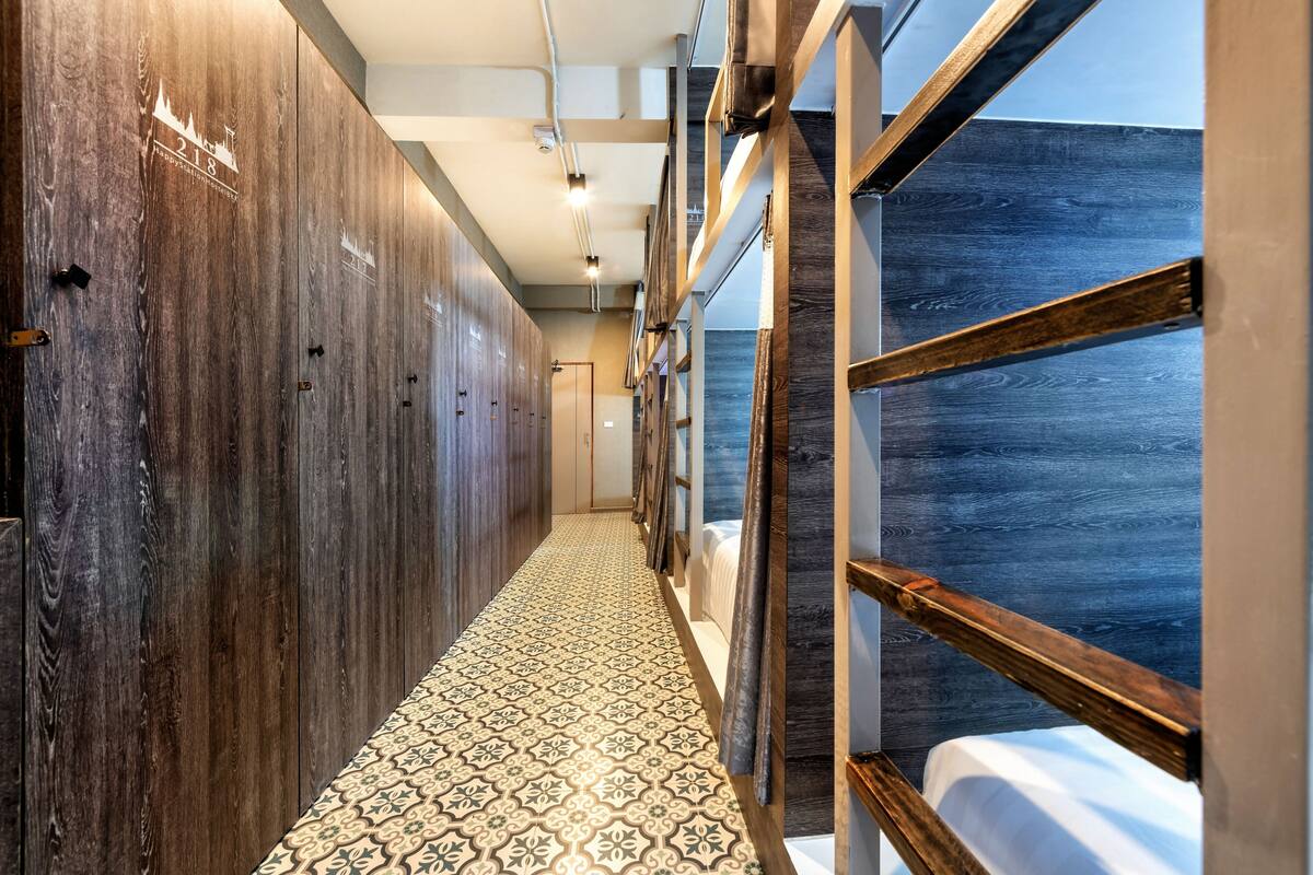 Corredor de hotel com paredes de madeira, pisos de azulejos estampados e vista para o mar através de uma janela.