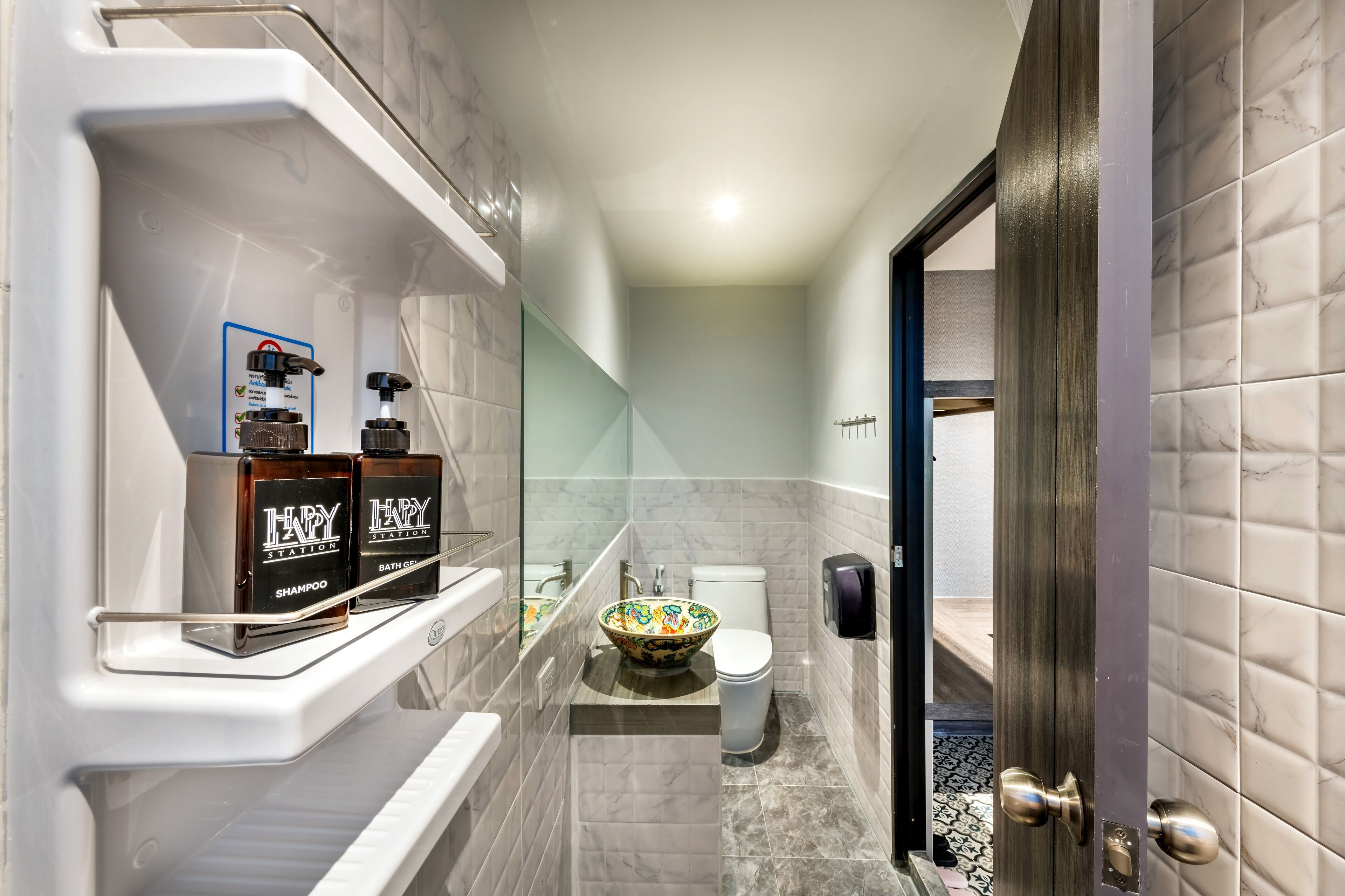 A modern bathroom with a bathtub, a toilet, and a sink. There are two bottles of shampoo and a soap dispenser on the shelf.