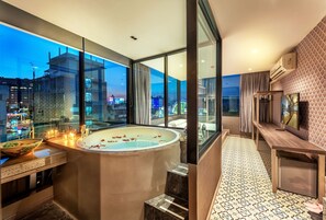 A modern bathroom with a large bathtub, a glass-enclosed shower, and a view of the cityscape at dusk. - Happy Station Bangkok (Bangkok)