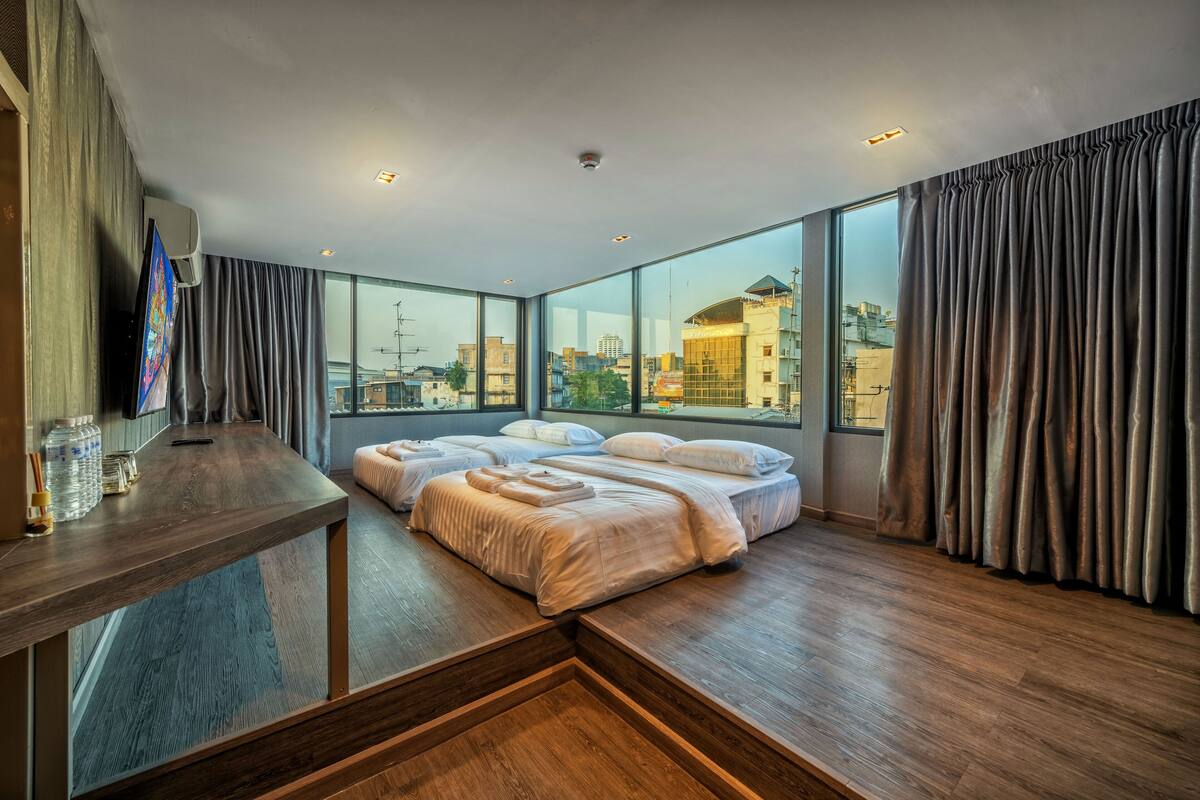 Quarto de hotel moderno com uma cama grande, uma escrivaninha com televisão de tela plana e vista para a cidade através de amplas janelas.