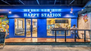 Fachada azul do Happy Station com um cardápio em lousa na parte externa.