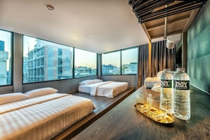 A hotel room with two beds, a large window with a city view, and a table with water bottles and glasses. - Happy Station Bangkok (Bangkok)