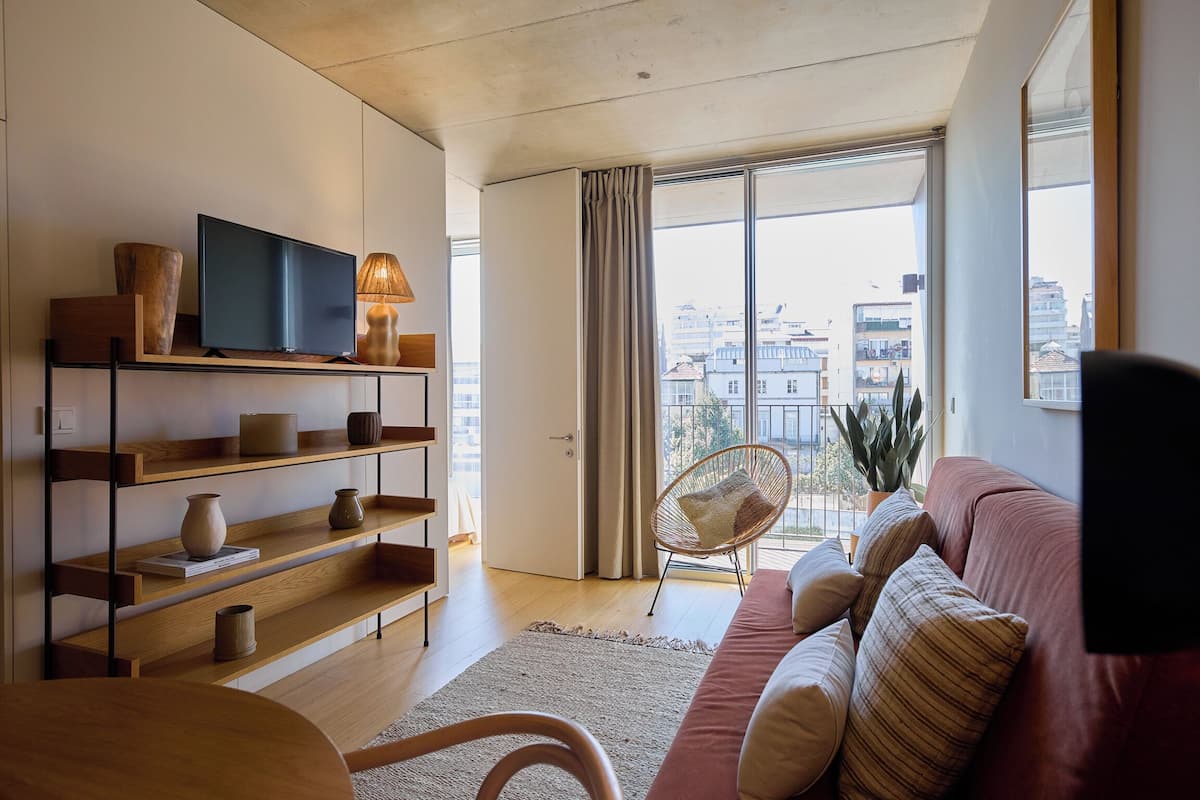 Una sala de estar moderna con un televisor de pantalla plana, estantes de madera, un sofá rojo y un ventanal con vistas a la ciudad.