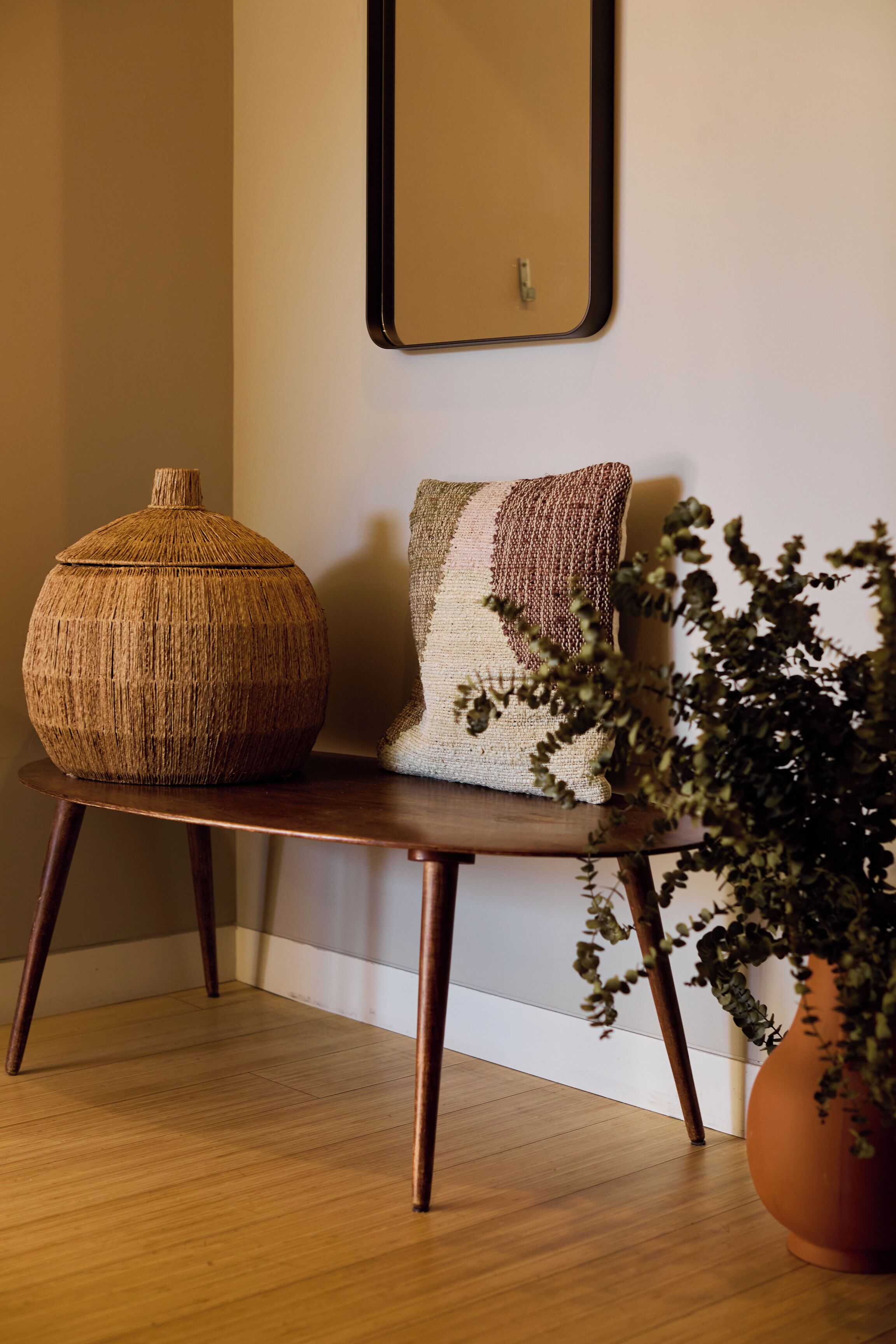 A wooden bench with a woven basket and a textured cushion against a wall.