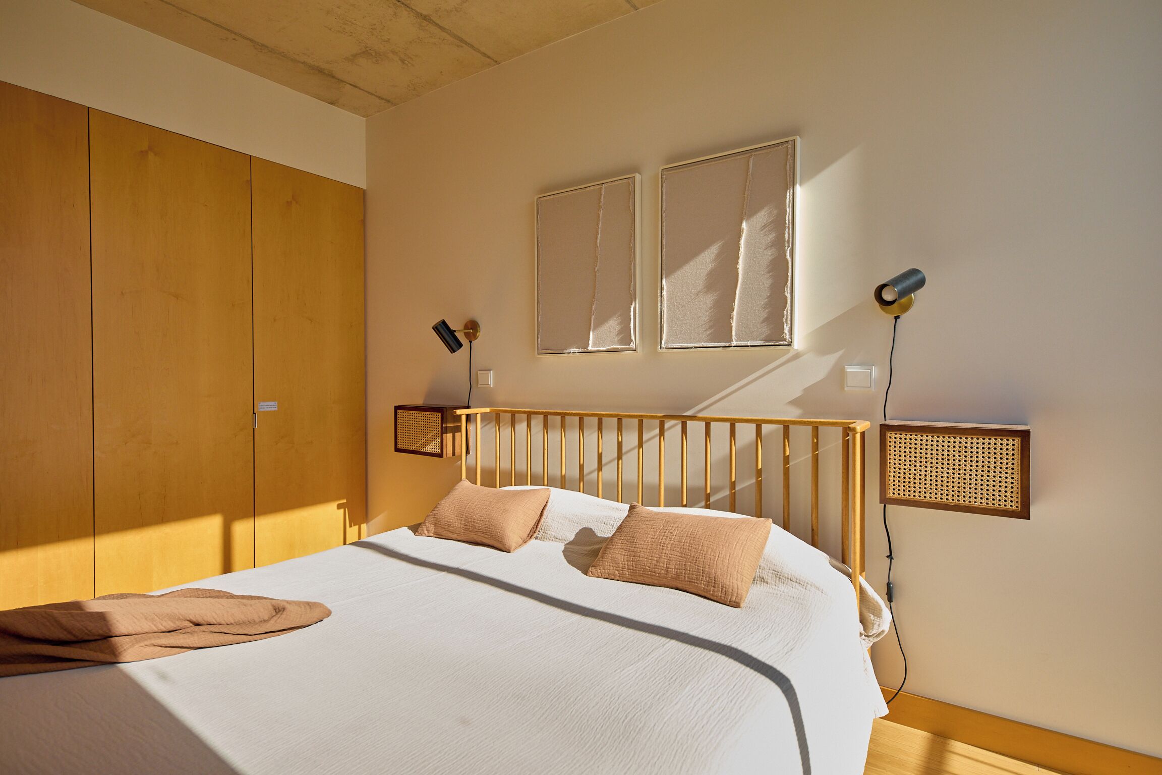 Un dormitorio con estructura de cama de madera, ropa de cama blanca y dos lámparas de noche.