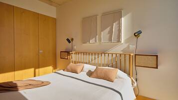 Un dormitorio con estructura de cama de madera, ropa de cama blanca y dos lámparas de noche.