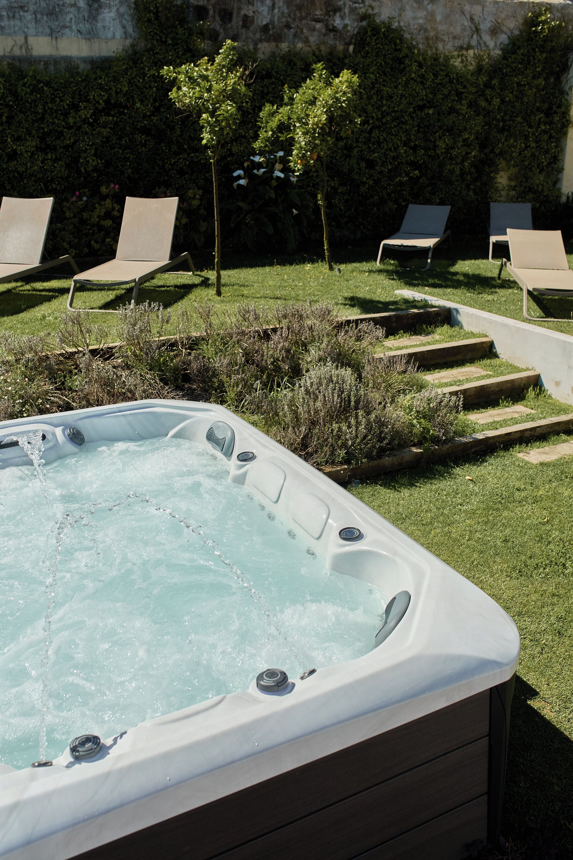 Un bain à remous avec une zone herbeuse et des chaises longues en arrière-plan.