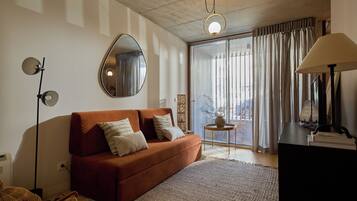 Un salon moderne avec un canapé, un miroir rond, une lampe sur pied et une vue à travers une grande fenêtre agrémentée de rideaux.