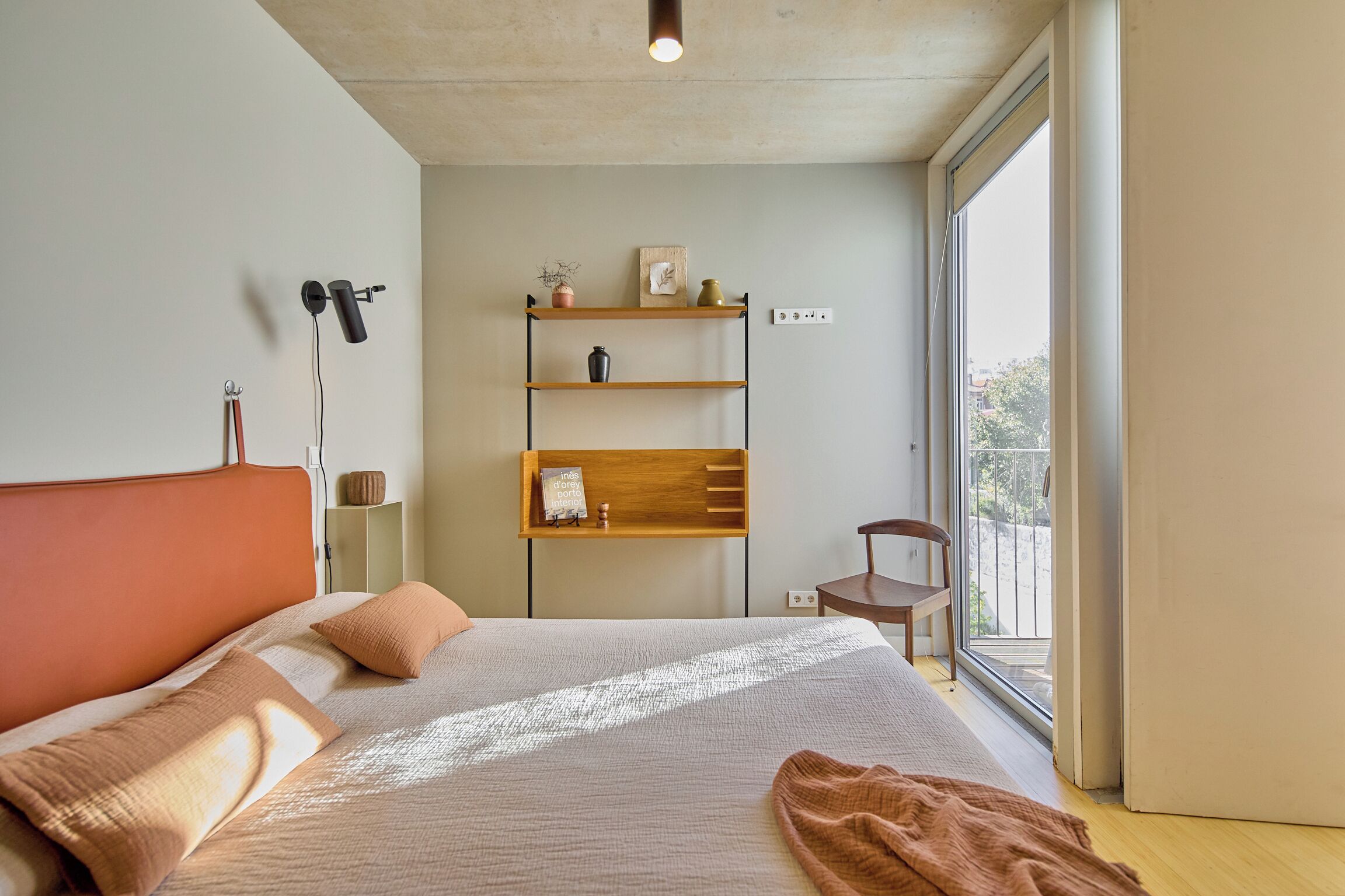 Ein modernes Schlafzimmer mit einem großen Bett, einer Holzhängeregals und Blick ins Freie durch ein großes Fenster.