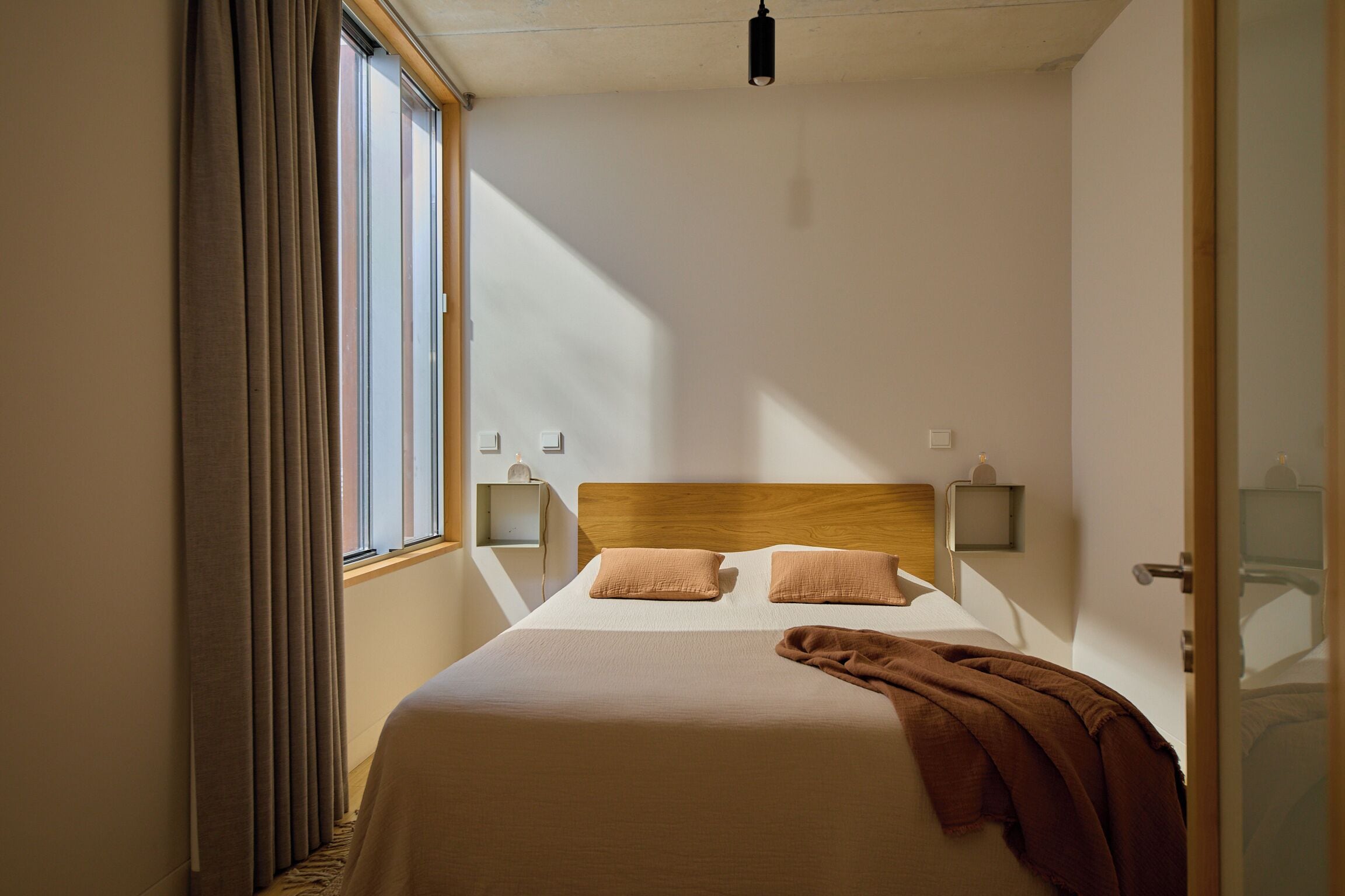 A neatly made bed with a wooden headboard, two bedside tables with lamps, and a window with curtains.