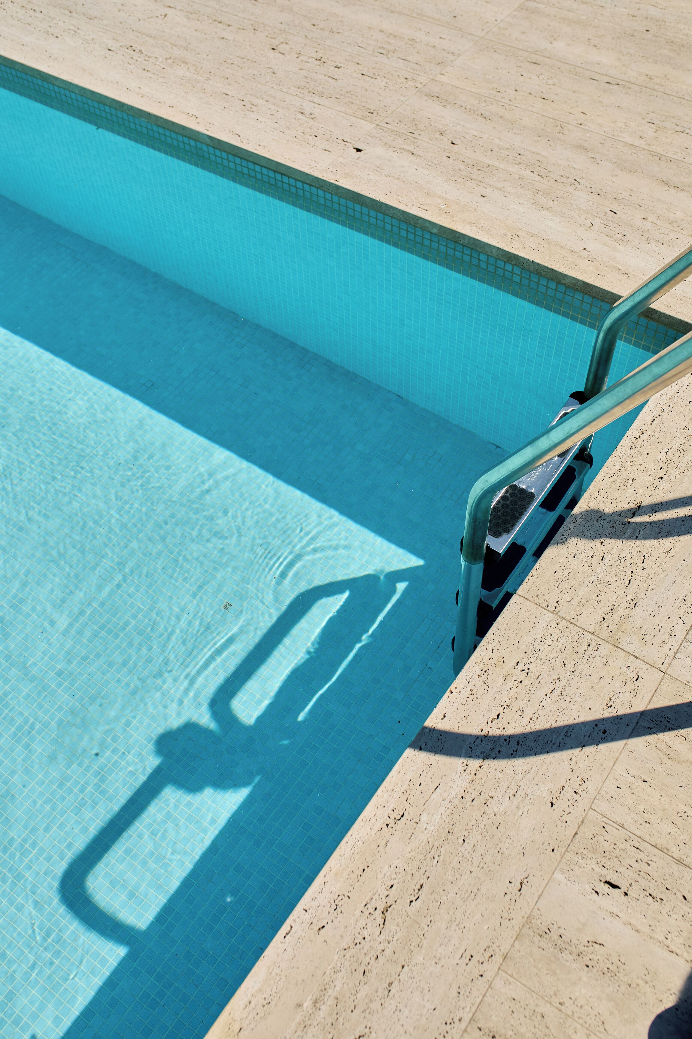 Une piscine à l’eau d’un bleu limpide, avec un bord carrelé et une rambarde métallique.