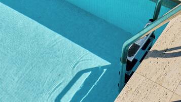Une piscine à l’eau d’un bleu limpide, avec un bord carrelé et une rambarde métallique.