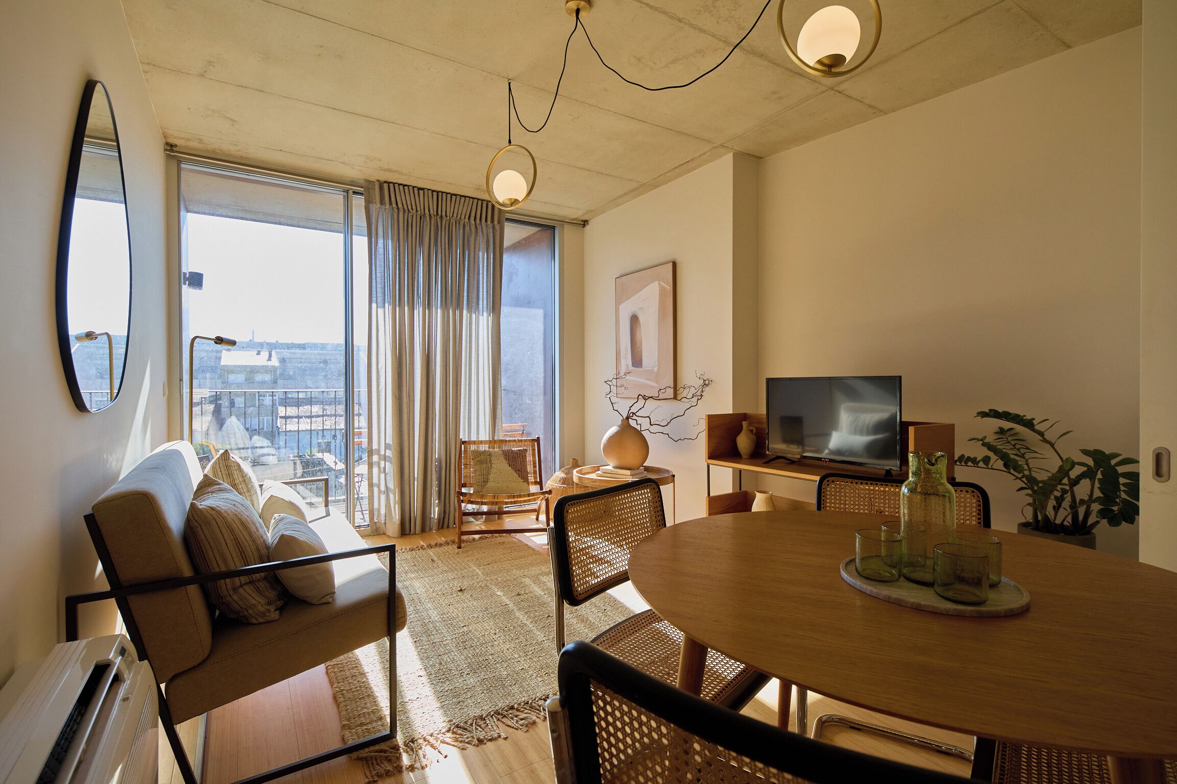 A modern living room with a sofa, dining table, chairs, a TV, and a large window with curtains.