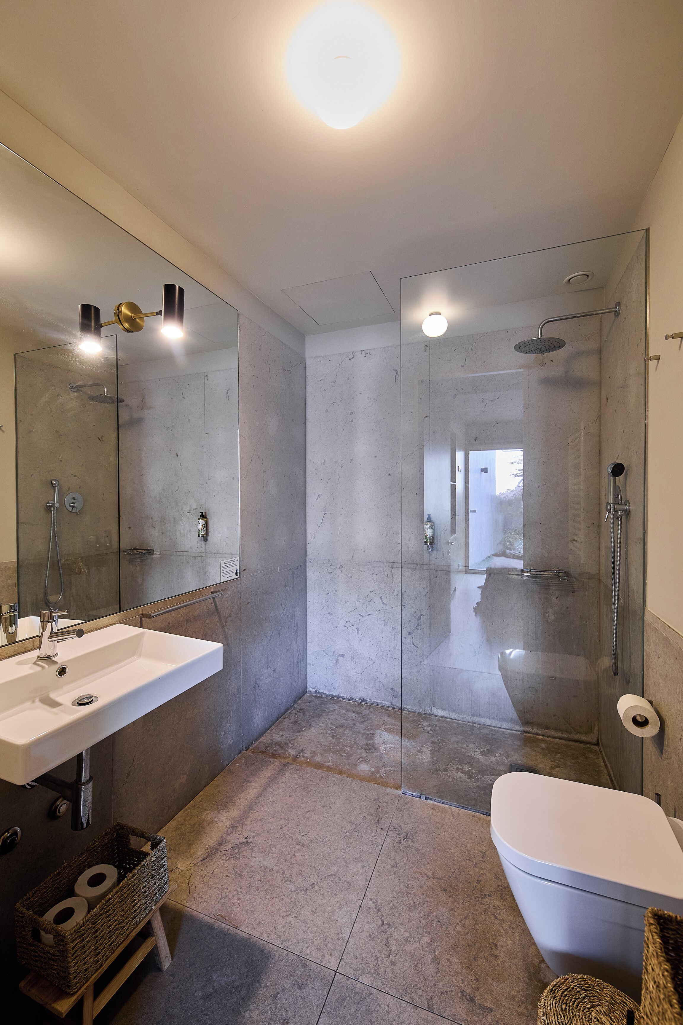 Une salle de bain moderne avec un lavabo blanc, un miroir et des toilettes, ainsi qu’un espace de douche clos par des parois de verre.