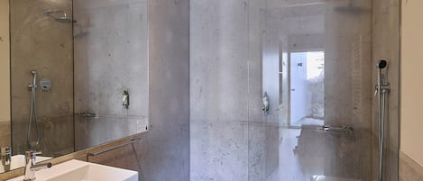 Un baño moderno con lavamanos, espejo y retrete blancos, y cabina de ducha con mampara de vidrio.