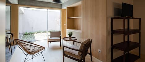 A modern living room with a wooden floor, a large window, and a dining area with a table and chairs.
