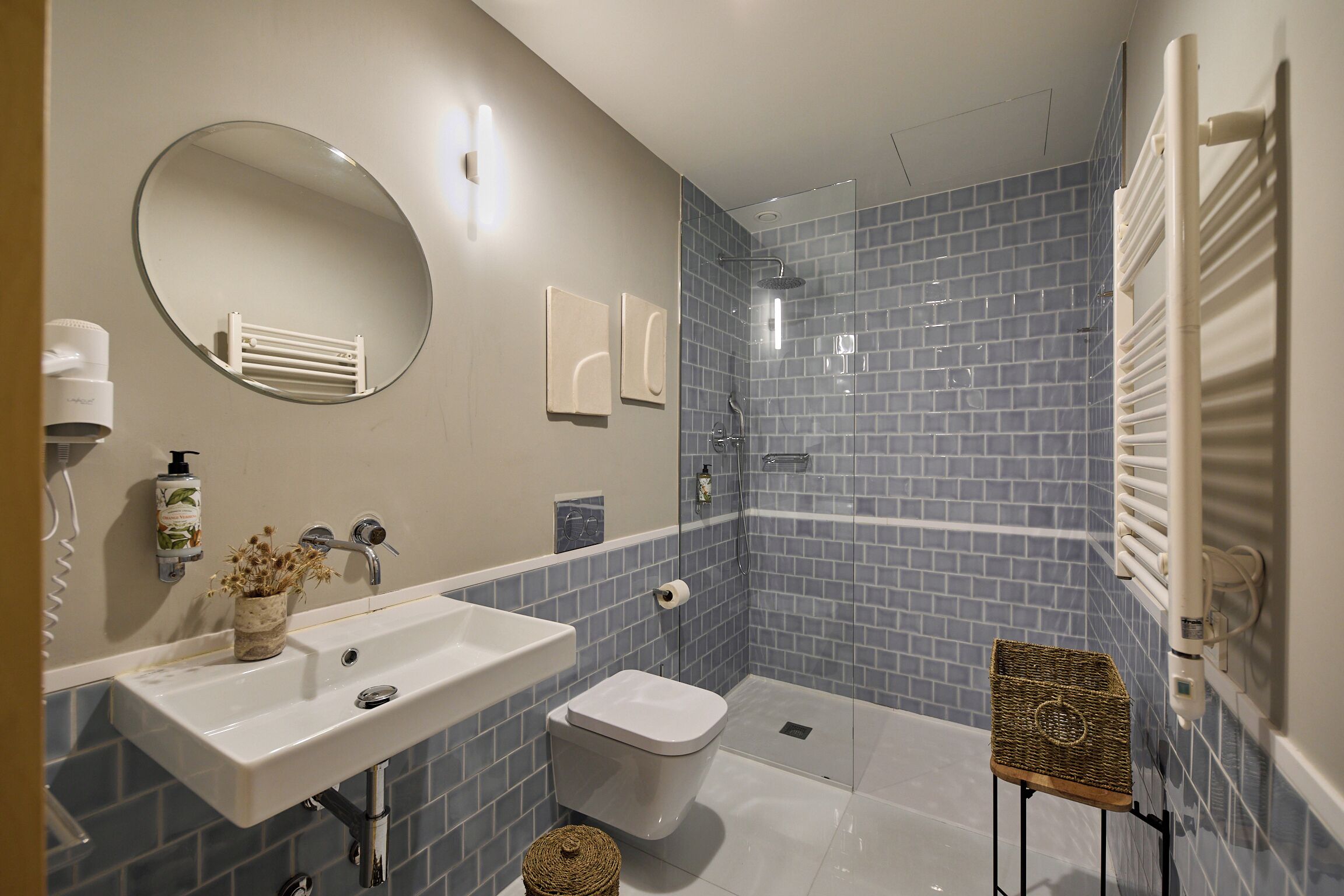 Ein Badezimmer mit Waschbecken, Toilette und Duschbereich, mit blau gefliesten Wänden und einem weißen Waschbecken.