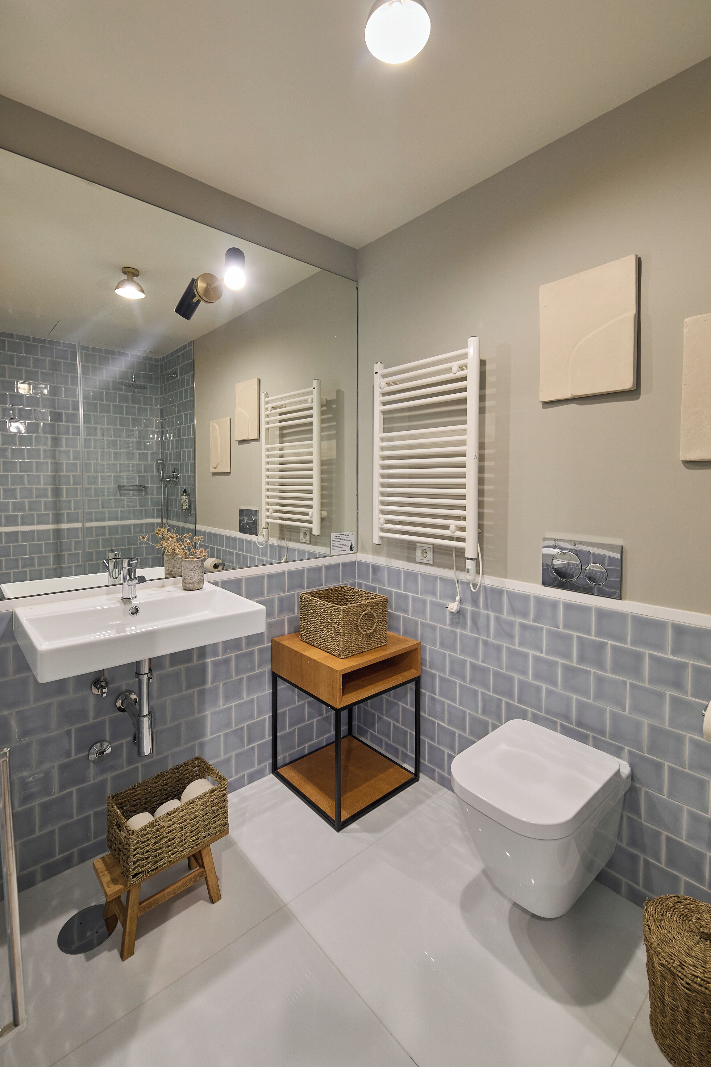 A modern bathroom with a white sink, a toilet, and a shower area. There are wicker baskets on the floor and a towel rack on the wall.